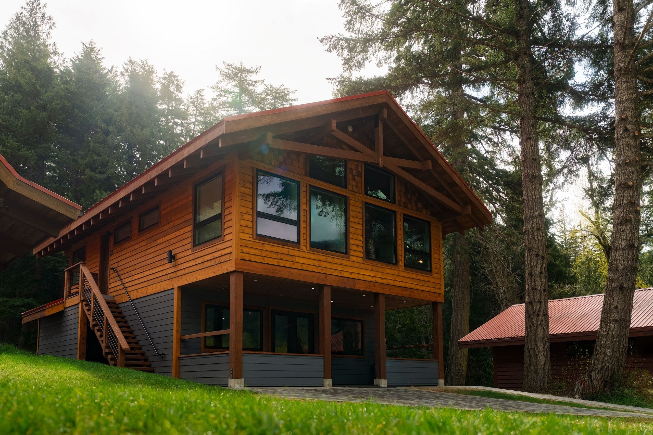A rustic family lodge at Tweedsmuir Park Lodge, showcasing a cabin with a deck and stairs amid lush forest surroundings.